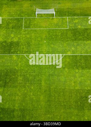 Aus der Vogelperspektive auf ein grünes Fußballfeld mit weißen Markierungen und einem einzigen Torpfosten. Das Gras zeigt Mähmuster, die eine gestreifte Textur erzeugen Stockfoto