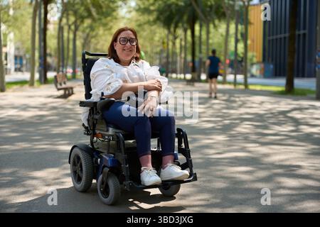 Lächelnde Frau mit elektrischem Rollstuhl, die einen sonnigen Tag im Park genießt - Rollstuhl- und Behindertenkonzept Stockfoto