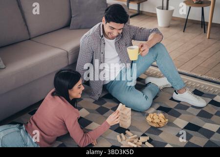 Junges Paar, das sich zu Hause die gemeinsame Freizeit gönnt und sich bei einem Spiel verbündet, während es Snacks und Getränke in einem gemütlichen Wohnzimmer genießt. Stockfoto
