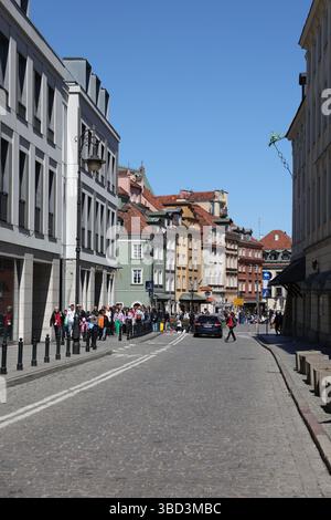 Touristen wandern an einem sonnigen Tag entlang einer farbenfrohen Kopfsteinpflasterstraße in der Altstadt von Warschau, Polen, mit historischen Gebäuden im Hintergrund. Stockfoto
