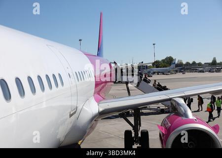 Auf dem Rollfeld des Flughafens parkt ein kommerzielles Flugzeug mit markantem rosafarbenem Schwanz und Motor, während die Passagiere über eine mobile Treppe einsteigen. Das geschäftige Ai Stockfoto