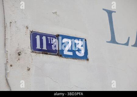 Zwei Straßenschilder sind an einer weißen Wand mit sichtbaren Rissen und abblätternder Farbe angebracht. Auf dem Schild links steht die Aufschrift „11 TER“ in weißem Text auf blauem Hintergrund Stockfoto
