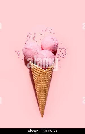 Erdbeerrosa Eiskügelchen mit Streuseln in Waffelkegel auf rosa Pastellhintergrund, kreatives Design mit hartem Licht, Kopierraum. Sommerbeere i Stockfoto