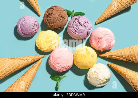 Verschiedene Eiskugeln und Waffelkegel kreativ flach auf blauem Hintergrund, Draufsicht. Verschiedene Eissorten oder trendiges Eis-Design. Stockfoto