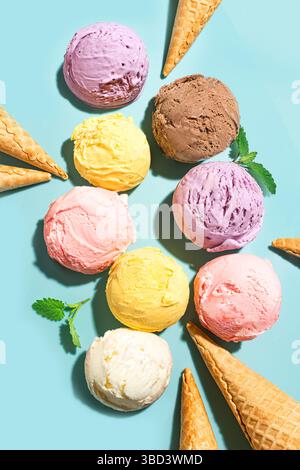 Verschiedene Eiskugeln und Waffelkegel kreatives Layout auf blauem Hintergrund, Draufsicht. Verschiedene Eissorten oder trendiges Eis-Design. Stockfoto