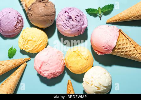 Verschiedene Eiskugeln auf blauem Hintergrund, Draufsicht. Verschiedene Eissorten oder Eis mit Waffelkegel, gesundes Sommerdessert kreatives Konzept. Stockfoto