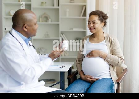 Schwangerschaft und Medizin. Schwarzer Gynäkologe, der jungen Schwangeren Pillen gibt Stockfoto