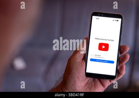 Bayern, Deutschland - 22. Mai 2025: FOTOMONTAGE, Startbildschirm der YouTube-App auf einem Smartphone - das rote Wiedergabesymbol erscheint zusammen mit dem Willkommenstext Willkommen bei YouTube. *** FOTOMONTAGE, Startbildschirm der YouTube-App auf einem Smartphone das rote Wiedergabe-Symbol erscheint zusammen mit dem Begrüßungstext Willkommen bei YouTube. Stockfoto