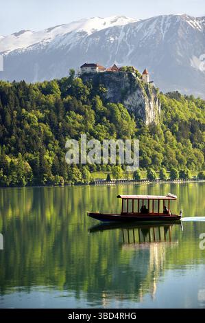 Ein Flachbodenboot namens Pletna auf dem Bleder See mit der Burg Bled und den alpen auf der Rückseite, Bled, Slowenien Stockfoto