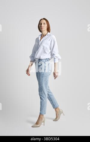 Trendige Seniorin, die in einem grauen Studio läuft Stockfoto