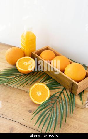 Eine ausgewogene Top-down-Komposition mit frischen Orangen, einer Flasche Saft, Palmblättern und einer Topfpflanze auf einer warmen Holzoberfläche. Die Stockfoto