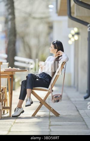 Nachdenkliche junge Frau, die an sonnigem Tag auf der Terrasse des Cafés sitzt und Kaffee trinkt Stockfoto