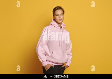 Stilvoller junger Mann in rosa Schweißaufnahme mit Kapuze, die auf gelbem Studiohintergrund posiert Stockfoto