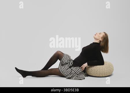 In voller Länge Studio Porträt von jungen Wooman auf dem Boden sitzen im Profil über grauem Hintergrund Stockfoto