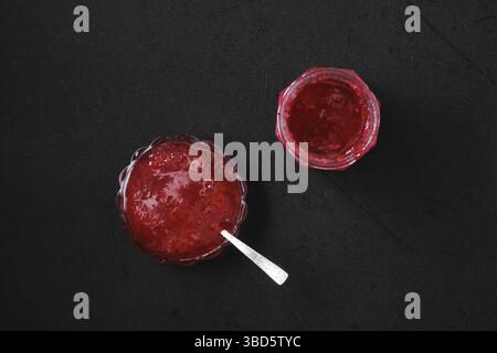 Draufsicht auf Glas und Untertasse mit Kirschmarmelade auf schwarzem Hintergrund Stockfoto
