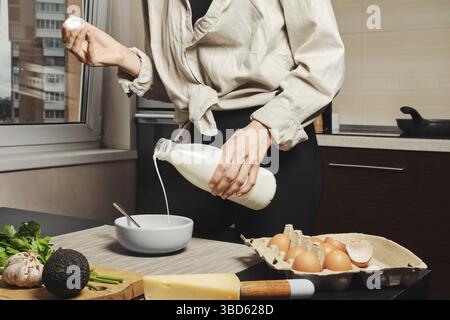 Unerkennbare Frau, die Milch in Eier in eine Schüssel gießt Stockfoto