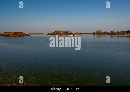 Die Küste der Chausey-Inseln während eines wunderschönen blauen Himmels und sonnigen Tages und bei Ebbe, während ein Motorboot vorbeischwingt. Chausey-Inseln, Normandie, Fra Stockfoto