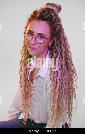 Junge Frau in einer Brille mit Dreadlocks unter Farblichtern Stockfoto
