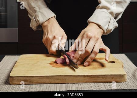 Unerkennbare Frau, die rohes Rindfleischfilet auf Schneidebrett schneidet Stockfoto