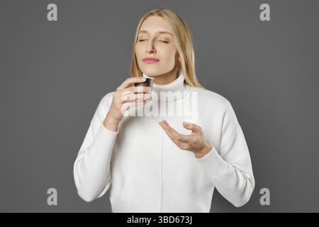 Eine junge Frau mit geschlossenen Augen hält eine Tasse frischen Kaffee in der Hand und atmet sein Aroma ein Stockfoto