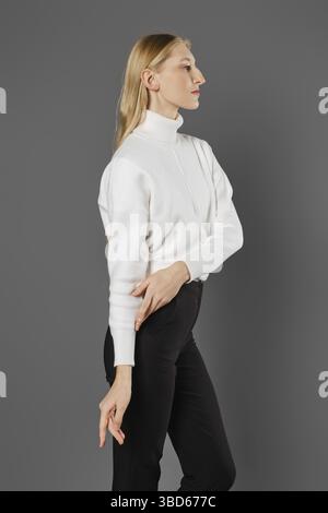 Eine junge Frau, die die Pullover-Ärmel hochzieht und im Profil steht Stockfoto