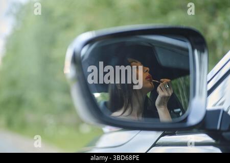 Spiegelung im Rückspiegel einer Frau, die im Auto einen Lippenstift anwendet Stockfoto