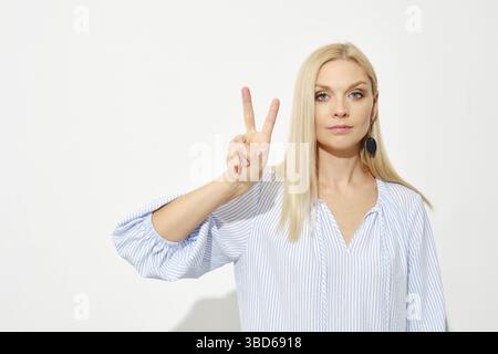 Eine attraktive blonde Frau zeigt zwei Finger. Mit den Fingern zählen Stockfoto