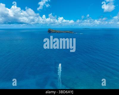 Blick auf ein entferntes Schnellboot mit hoher Drohne, das einen langen Weg auf offenem Meer verlässt, Coin de Mire sichtbar Stockfoto