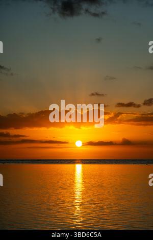 Ein lebendiger goldener Sonnenuntergang spiegelt sich über einem ruhigen, flachen Meer mit orangefarbenem Himmel Stockfoto