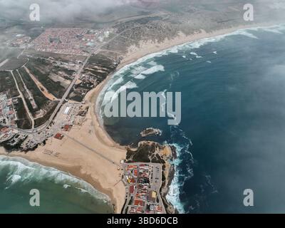 Breite Antenne mit Strandkrümmung, Wellen und Stadt, die sich ins Landesinnere ausdehnt Stockfoto