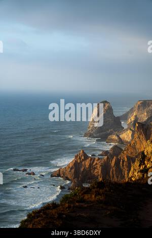 Die felsigen Klippen von Praia da Aroeira leuchten im warmen Licht bei Sonnenuntergang über dem Atlantik Stockfoto
