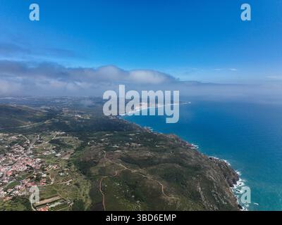 Breites Luftpanorama eines Küstendorfes in der Nähe von üppigen Hügeln und weitläufigen blauen Gewässern des Atlantiks Stockfoto