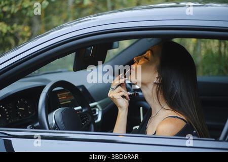 Stylische Frau, die Lippenstift anklebt, während sie im Auto sitzt Stockfoto