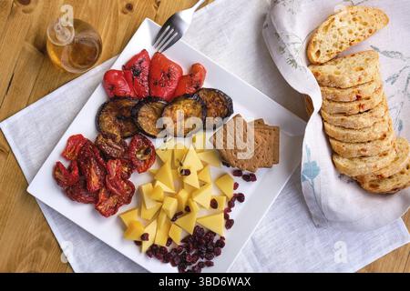 Blick von oben auf verschiedene Vorspeisen für Wein, Käse, sonnengetrocknete Tomaten, geröstete Auberginen, Paprika, Hardtack und getrocknete Preiselbeere Stockfoto
