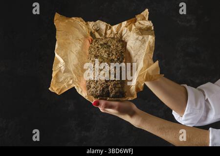 Weibliche Hände halten Hackbraten in Geschenkpapier in den Händen Stockfoto