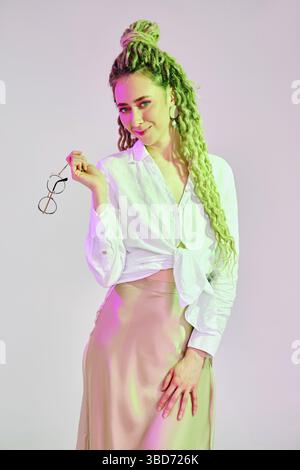 Fröhliche Frau spielt mit einer Brille unter bunten Lichtern im Studio Stockfoto