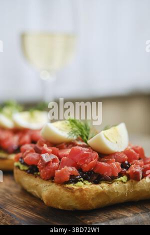 Frisch zubereitete Sandwiches mit offenem Gesicht umfassen leuchtende Lachsbrocken auf Avocado- und Zwiebelpüree. Genießen Sie dieses Gericht zusammen mit einem Glas Weißwein Stockfoto
