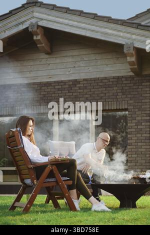 Glückliches Paar, das draußen grillt. Mann, der Würstchen auf dem Grill dreht Stockfoto