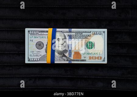 Stapel Dollar mit Band in Farben der ukrainischen Flagge auf schwarzem Hintergrund, Finanzen und Wirtschaft Stockfoto