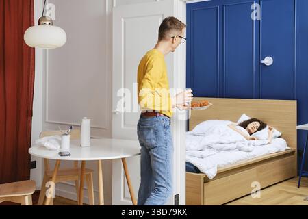 Ein Mann bringt seiner schlafenden Frau Frühstück ins Bett Stockfoto