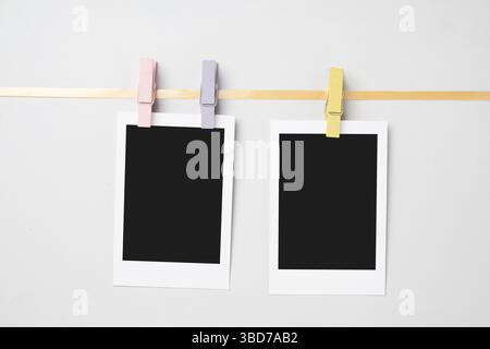 Zwei leere Polaroid-Fotopapiere mit Kleiderschalen, die am Seil hängen, mit weißem Hintergrund. Modell, Vorlage oder Kopierbereich. Sofortaufnahme der Kamera Stockfoto