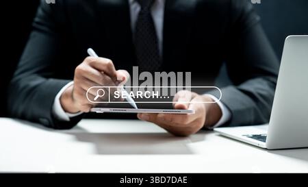 Geschäftsmann, der ein Tablet verwendet und ein Symbol für die Suchmaschinenleiste auf dem Bildschirm anzeigt. Laptop auf dem Schreibtisch. Technologische Innovation auf dem virtuellen Bildschirm. Concep Stockfoto