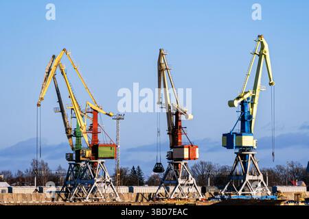 Schwere Kräne arbeiten an einem belebten Ort am Wasser an einem sonnigen Tag im Frachtumschlag. Stockfoto
