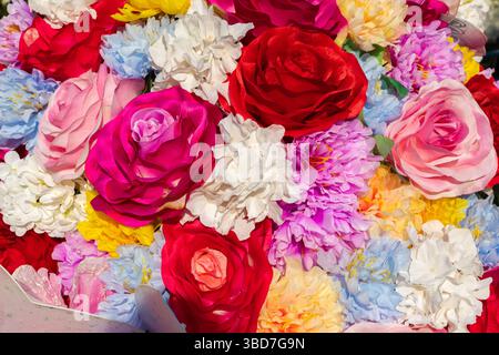 Lebendige Nahaufnahme verschiedener Kunstblumen in verschiedenen Farben, die ein fröhliches und dekoratives Blumenarrangement schaffen. Stockfoto
