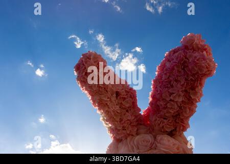 Dekorative Hasenohren aus rosa Kunstblumen mit blauem Himmel und Wolken im Hintergrund, perfekt für Frühlings- oder Ostermotive. Stockfoto