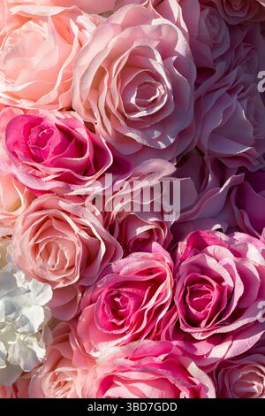 Weiche rosa und magentafarbene künstliche Rosen in Nahaufnahme bilden einen romantischen floralen Hintergrund mit eleganter Textur und Farbe. Stockfoto