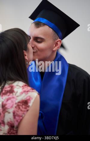 Ein abgeschlossenes Paar teilt sich einen Kuss während der akademischen Zeremonie in Kleid und Mütze Stockfoto