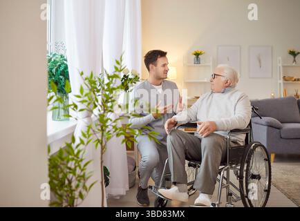 Junger Sozialarbeiter im Gespräch mit älteren behinderten Menschen im Rollstuhl. Stockfoto