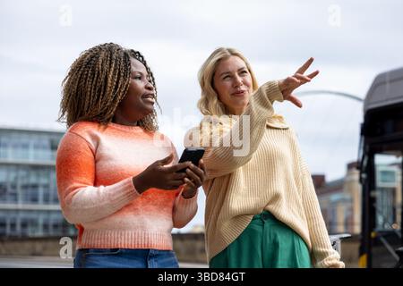 Vorderansicht von zwei mittelerwachsenen Freundinnen, die in einer Stadtstraße in Newcastle, England, stehen. Sie suchen nach Wegbeschreibungen, während sie eine intelligente p Stockfoto