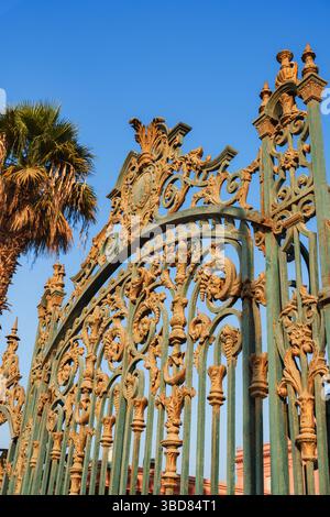 Verzierte Eisentore eines historischen Gartens, umgeben von Palmen unter einem klaren blauen Himmel Stockfoto
